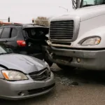 Multi-vehicle accident scene involving silver sedan, black SUV, and white semi-truck at an urban intersection